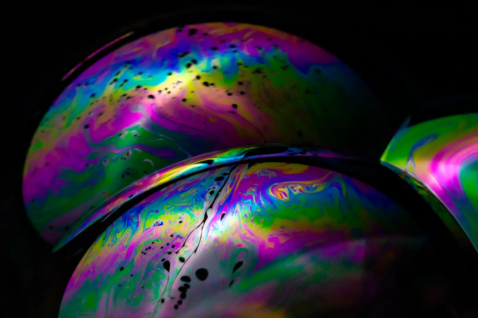 Gros plan sur la paroi de bulles de savon aux reflets violets, verts et jaunes, sur fond noir