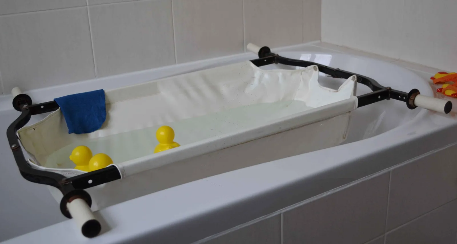 Baignoire pour bébé des années 1950 en toile tendue au-dessus d'une baignoire, avec de l'eau, des canards jaunes et une serviette bleue