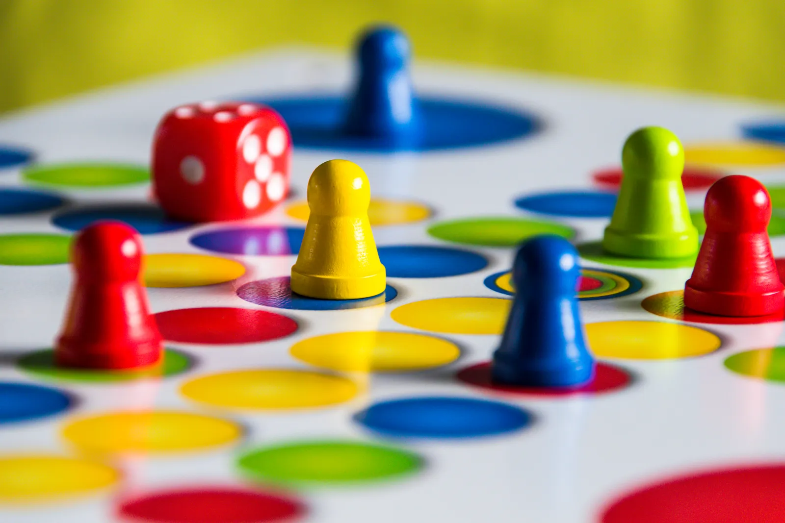 Pions de jeu de société rouges, jaunes, bleus et verts et un dé rouge posés sur un plateau couvert de pastilles de couleur
