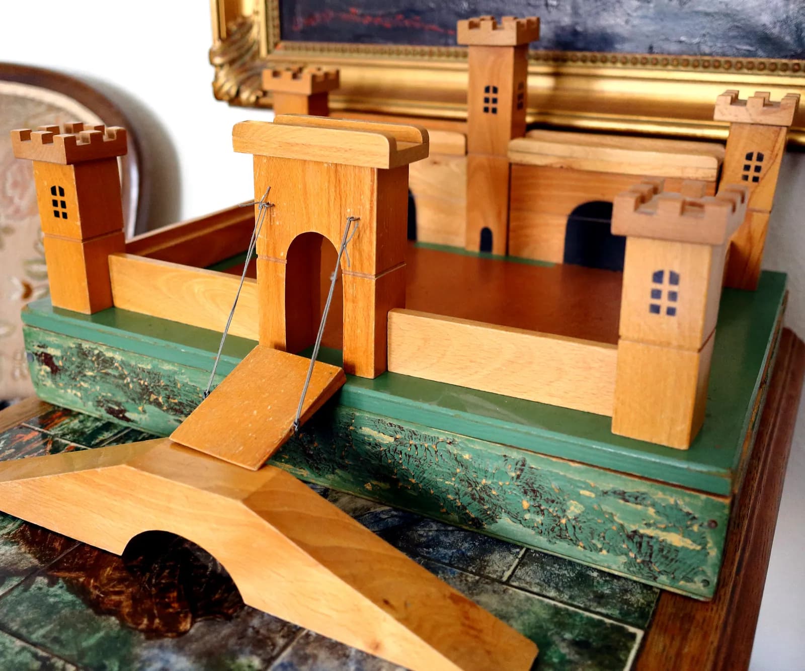 Château fort en bois ancien avec pont-levis et tourelles, posé sur une table devant un tableau au cadre doré