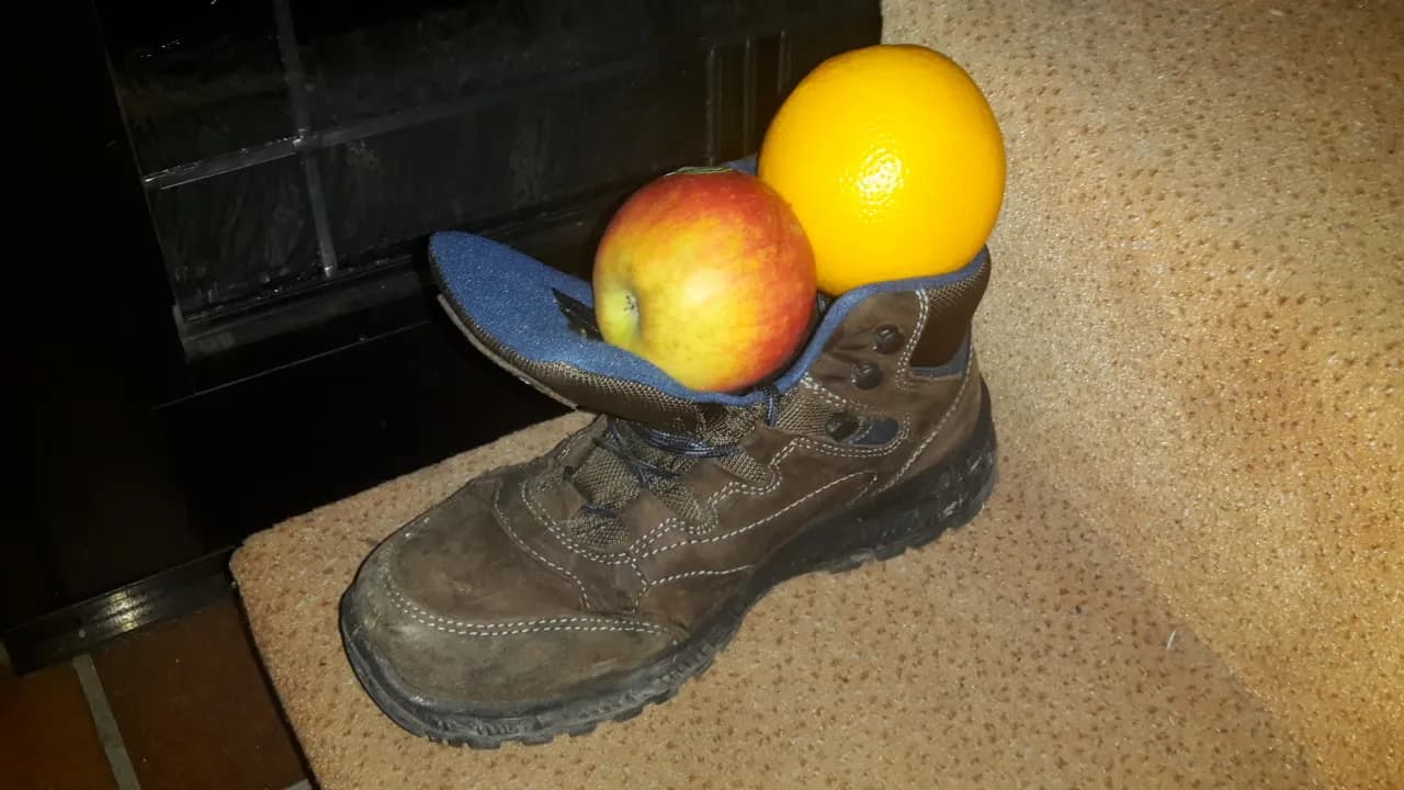 Chaussure de randonnée posée devant une cheminée, garnie d'une pomme et d'une orange pour la Saint-Nicolas