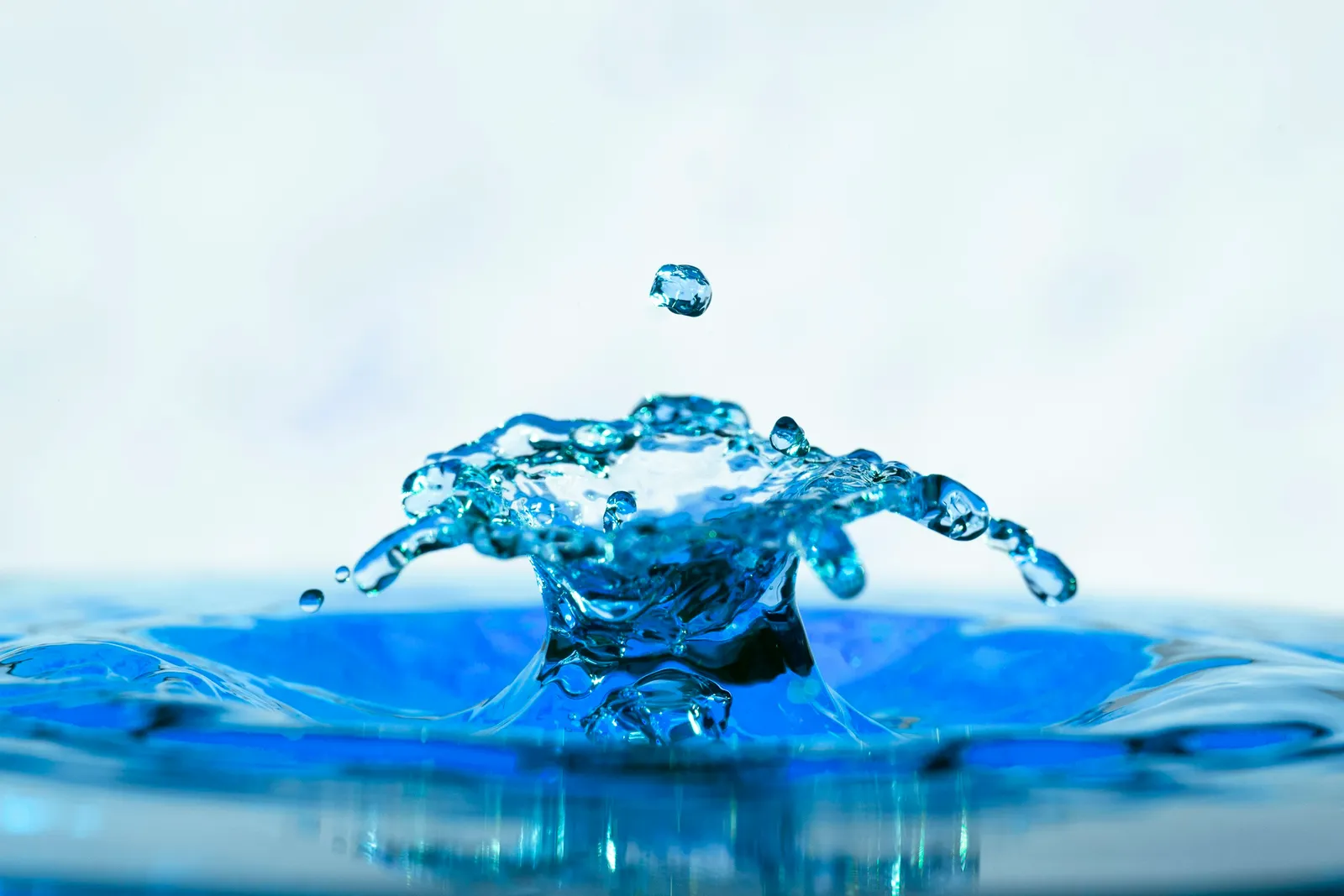 Goutte d'eau qui rebondit et forme une couronne d'éclaboussures sur une eau bleue