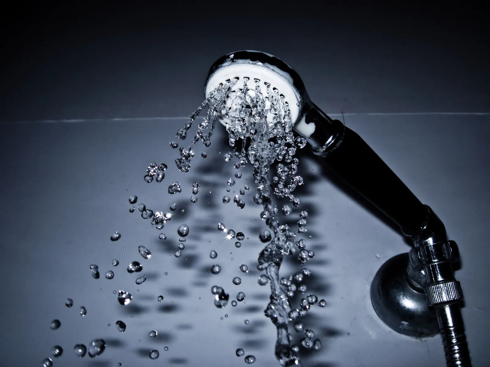 Pommeau de douche d'où jaillissent des gouttes d'eau, photographié en gros plan sur fond sombre