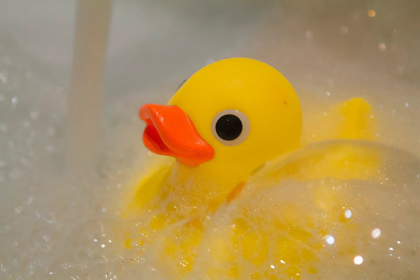 Canard en plastique jaune au bec orange qui flotte dans la mousse d'un bain