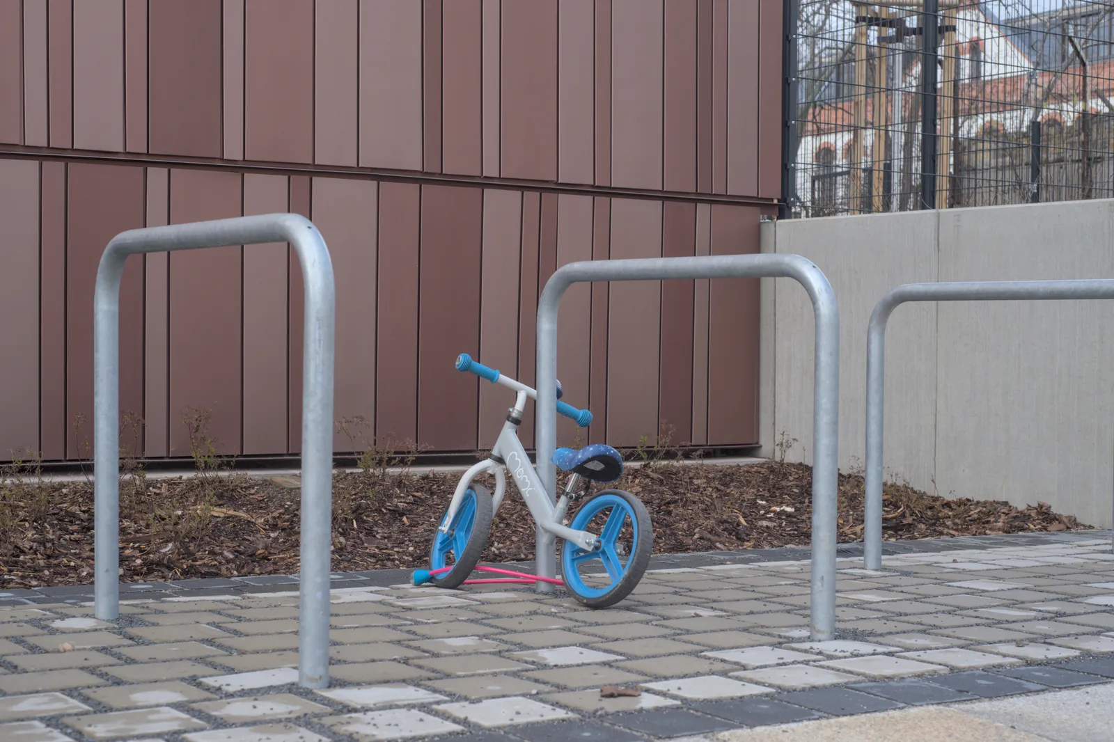 Draisienne d'enfant blanche et bleue garée contre un arceau à vélos devant un bâtiment
